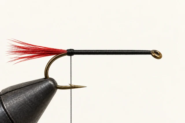 A black-threaded hook with a sparse red fiber tail; no body or hackle.