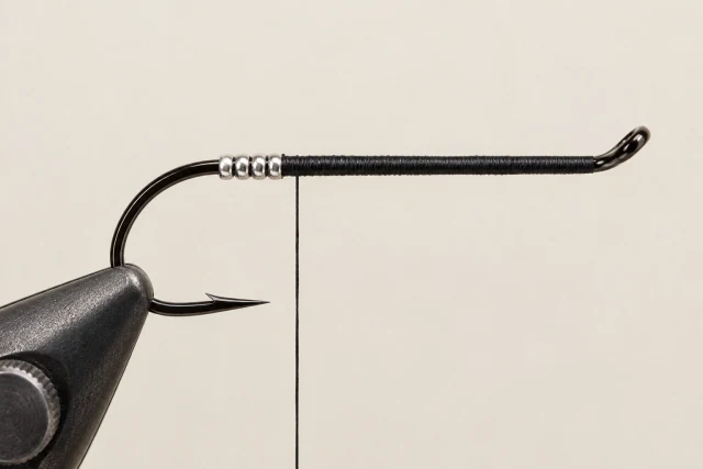 A black-threaded salmon single with a short silver tag near the bend; no tail or body.