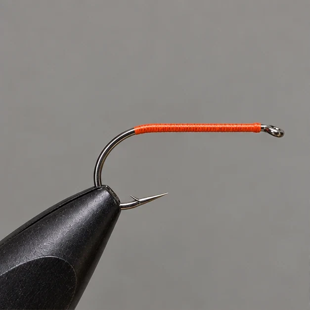 Orange thread foundation on a bare saltwater hook in a vise.