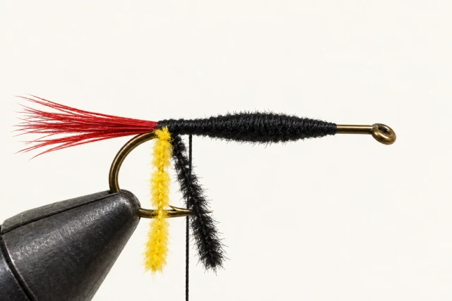 Black yarn underbody and two loose chenille strands, yellow and black, attached at the rear.